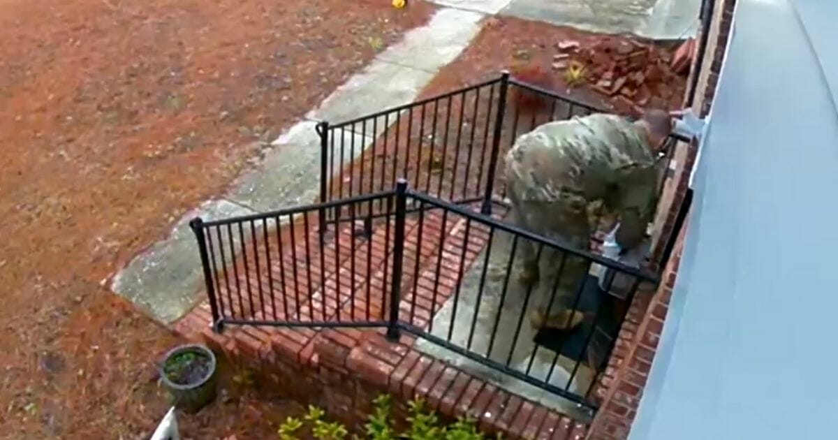 A man in fatigues folds a U.S. flag and places it on the doorstep.