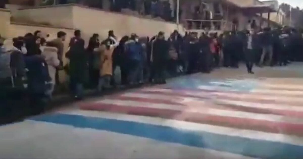 Protesters walk around U.S. and Israeli flags painted on a street in Tehran, Iran.