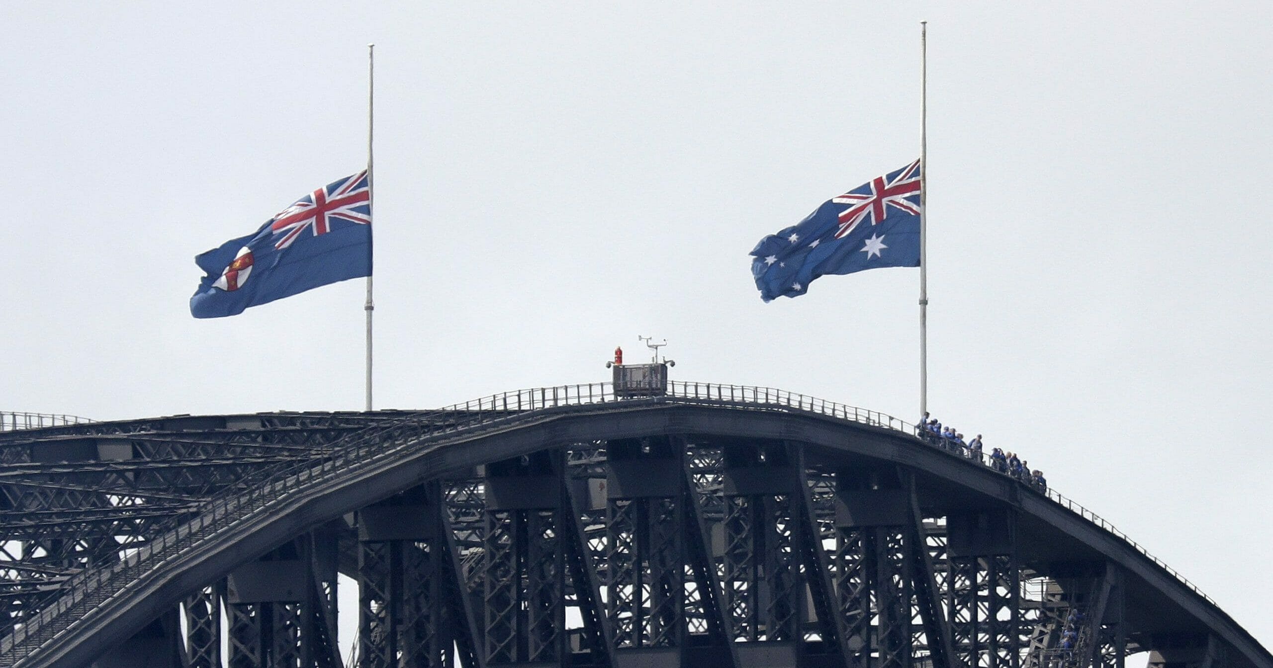 People climbing the Sydney Harbour Bridge stop under flags flying at half-mast as mark of mourning and respect in Sydney, Australia, on Jan. 24, 2020, for three U.S. crew members of an aerial water tanker that crashed while battling wildfires in Australia.