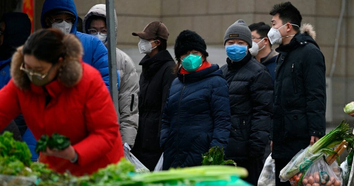 People wearing masks line up to pay for vegetables at an open market as snow falls in Beijing on Feb. 2, 2020.