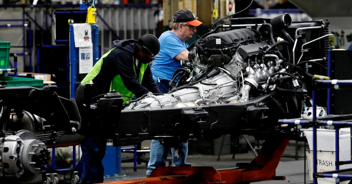 Line workers work on the chassis of full-size General Motors pickup trucks