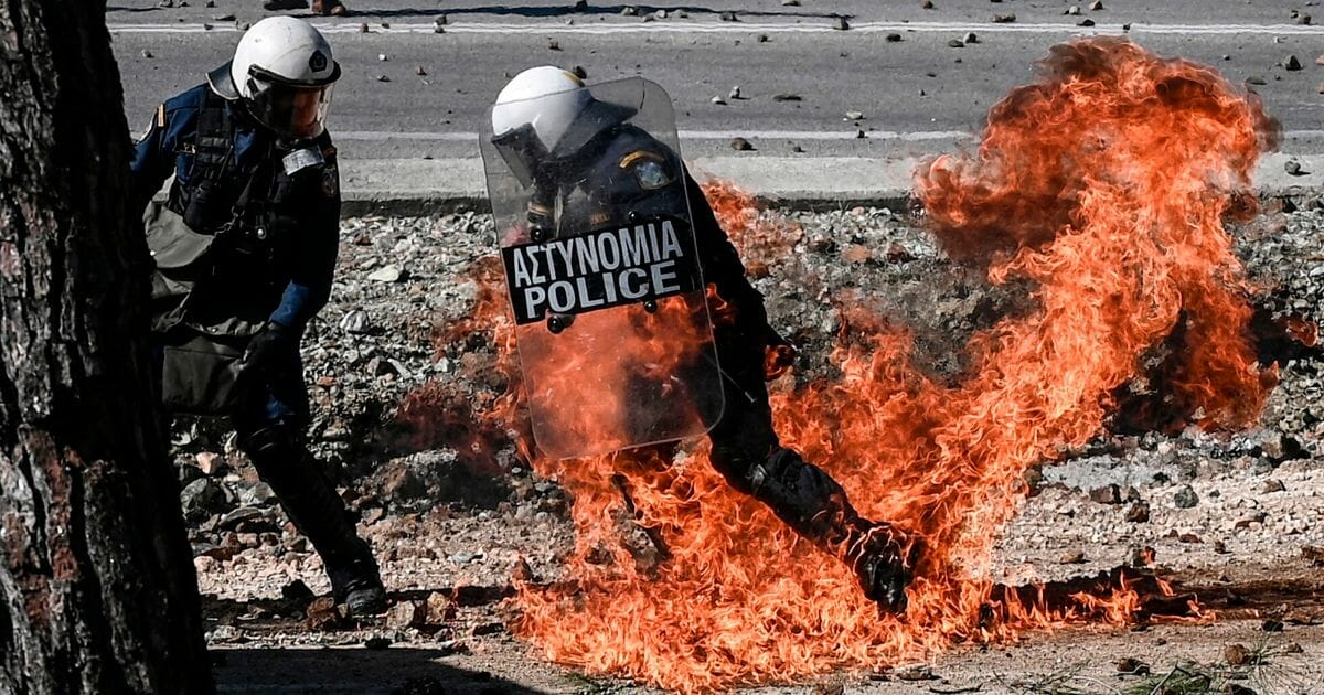 A Greek anti-riot police officer moves away from flames during clashes with demonstrators protesting against the construction of a controversial new migrant camp near the town of Mantamados on the northeastern Aegean island of Lesbos on Feb. 26, 2020.
