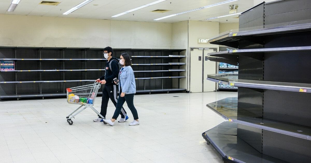 Shoppers wearing protective face masks walk past bare supermarket shelves, usually stocked with toilet paper and kitchen rolls, in Hong Kong on Feb. 6, 2020.