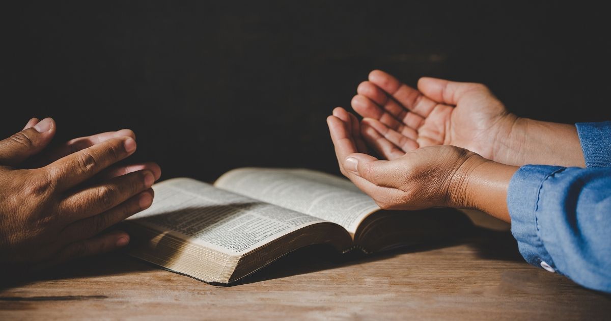 Stock image of people praying with a Bible.