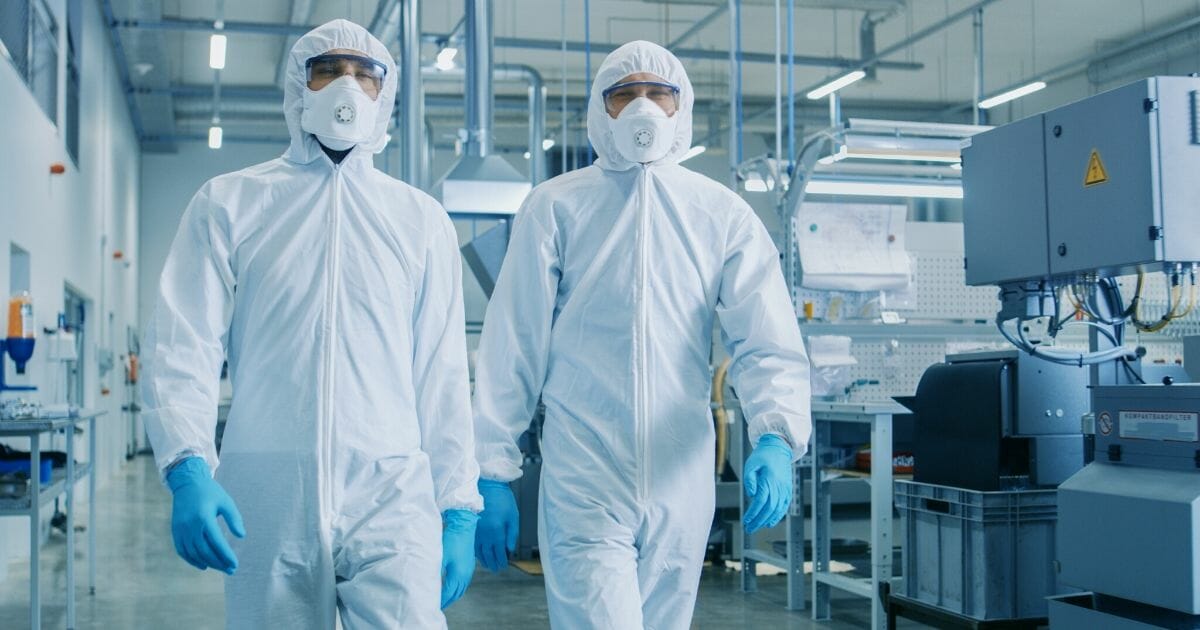 Stock image of two people in hazmat suits walking through a laboratory.