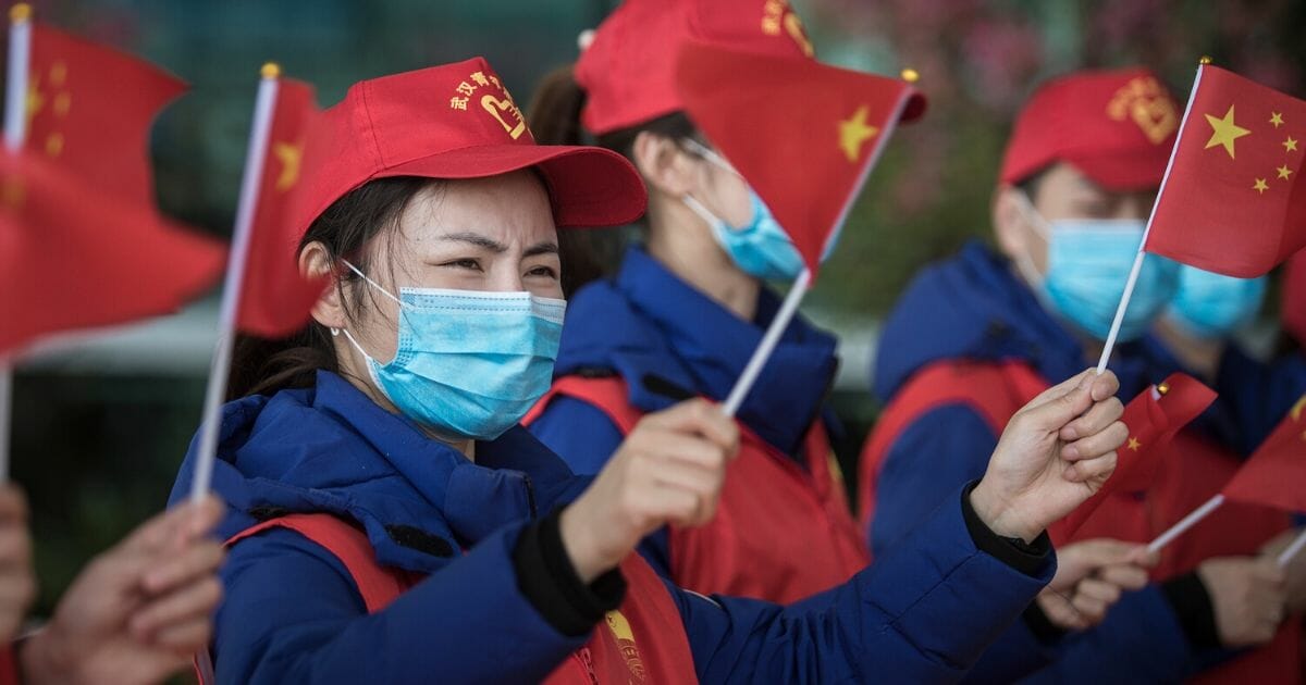 People in protective masks wave the Chinese national flag at the Tianhe airport in Wuhan on March 17, 2020.