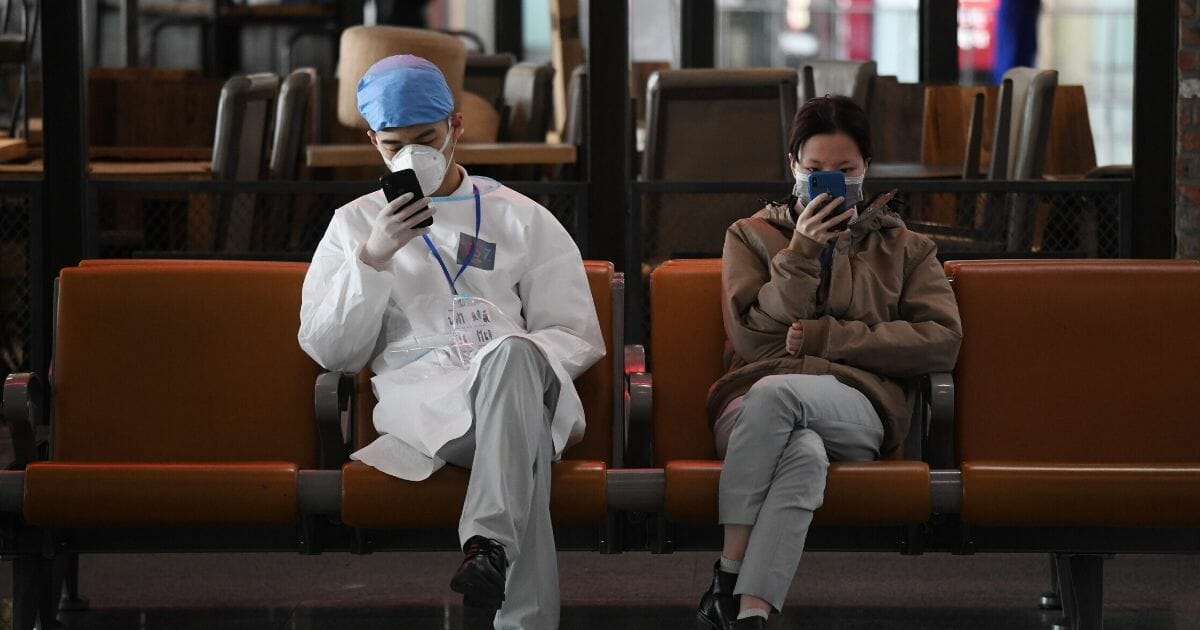 People look at their mobile phones in the empty arrivals area in Beijing Capital Airport on March 27, 2020
