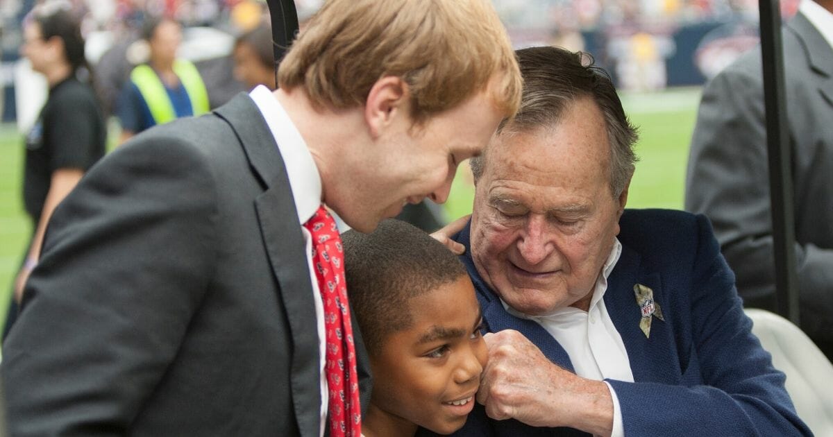 Former President George H.W. Bush, right, playfully gives a young man a fist to his face as his grandson Pierce Bush looks on at Salute To Service day before the Houston Texans play the Buffalo Bills at Reliant Stadium on Nov. 4, 2012, in Houston, Texas.