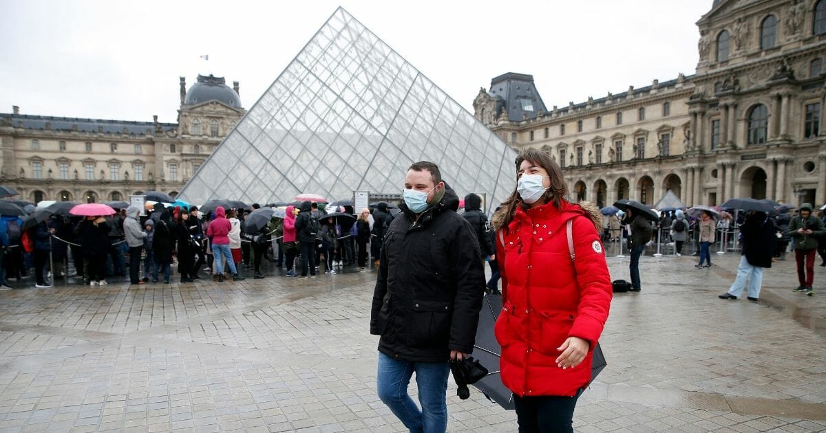 Tourists wearing protective masks walk past the Louvre in Paris on March 2, 2020.