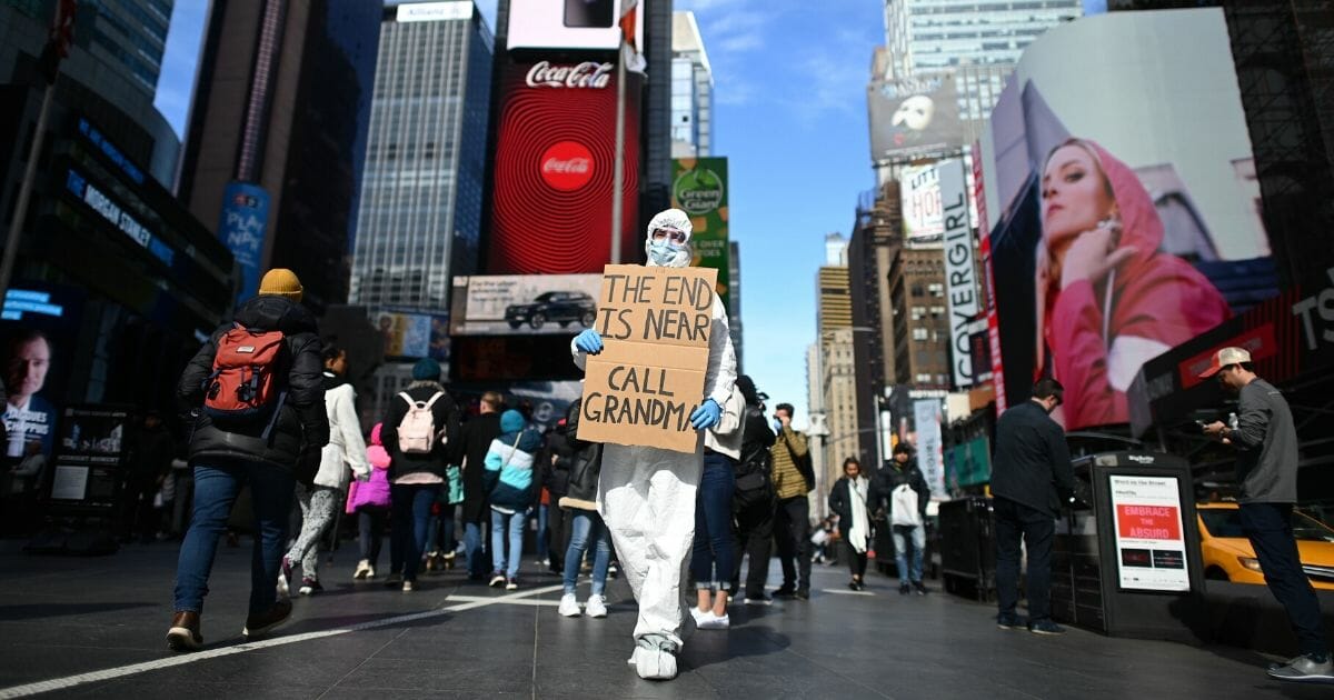 A man wearing a hazmat suit and a mask holds a sign at Times Square on March 14, 2020, in New York City.