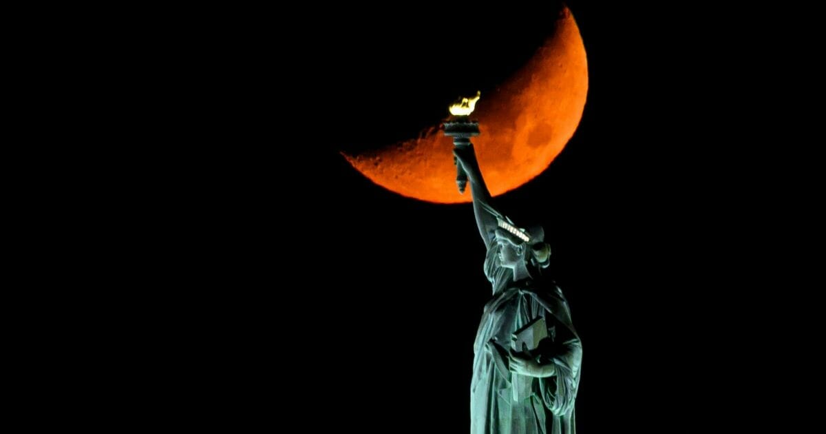 The moon sets behind the Statue of Liberty in New York on Nov. 2, 2019.