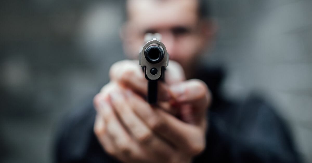 A man holds a handgun pointed at the camera.
