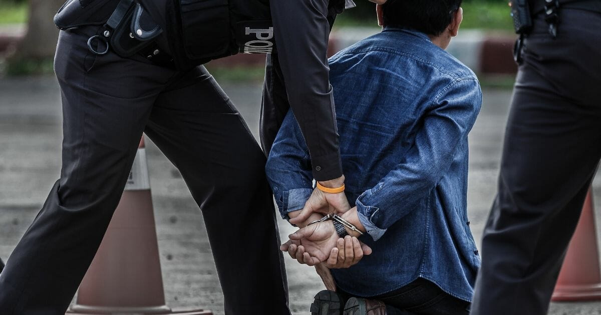 A man being handcuffed from behind by law enforcement.