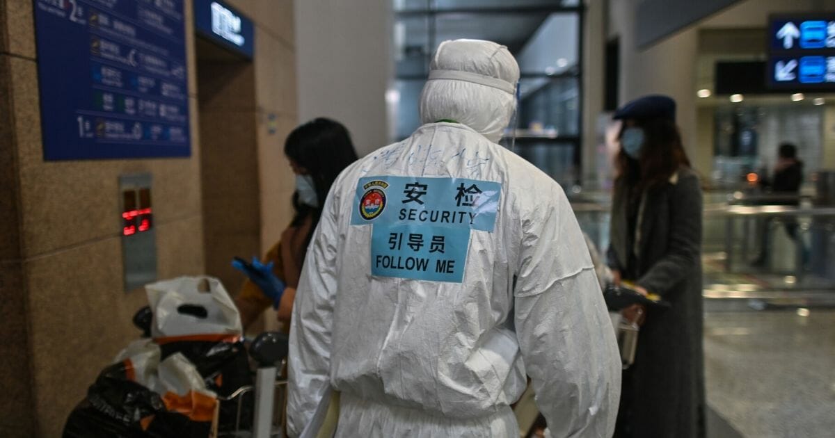 An airport security guard covered in protective gear against coronavirus infection escorts passengers to a bus at Shanghai Pudong International Airport in Shanghai on Thursday.