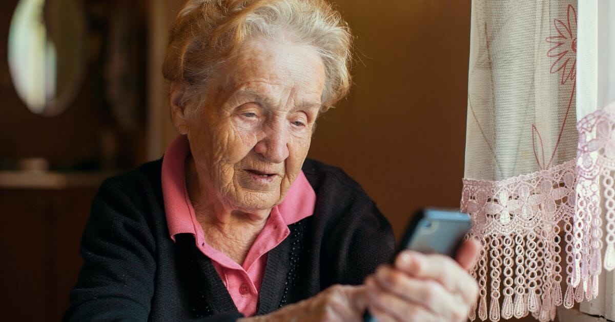 An elderly woman uses a phone in the stock image above.