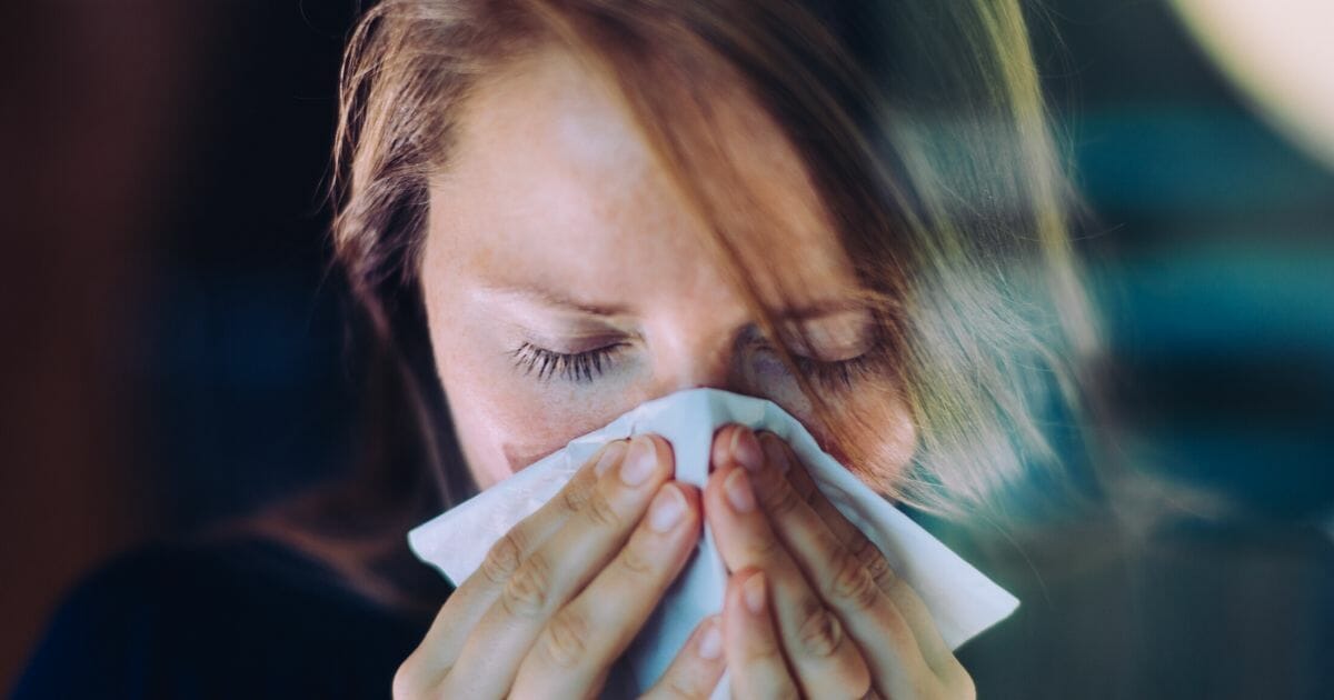 A stock photo of a woman sneezing is seen above.