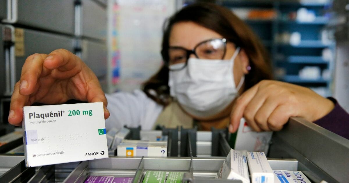 A pharmacy employee wearing a protective mask shows a box of Plaquenil (hydroxychloroquine) on March 27, 2020 in Paris.