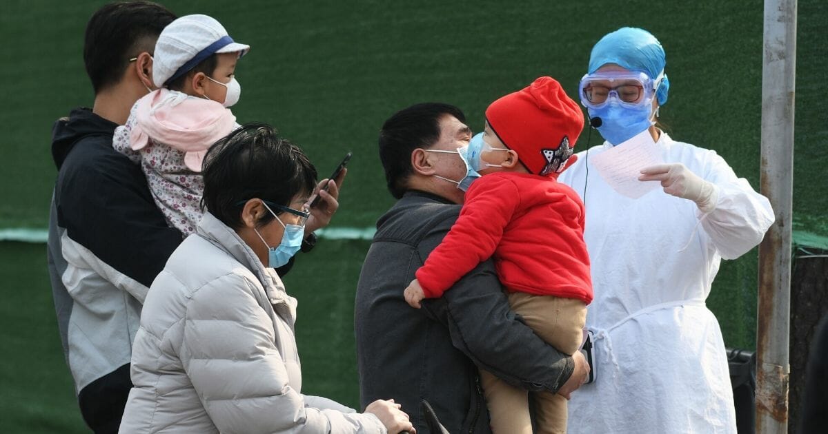 Families wait to enter a children's hospital near hospital staff wearing protective gear as a precautionary measure against the COVID-19 coronavirus in Beijing on March 31, 2020.