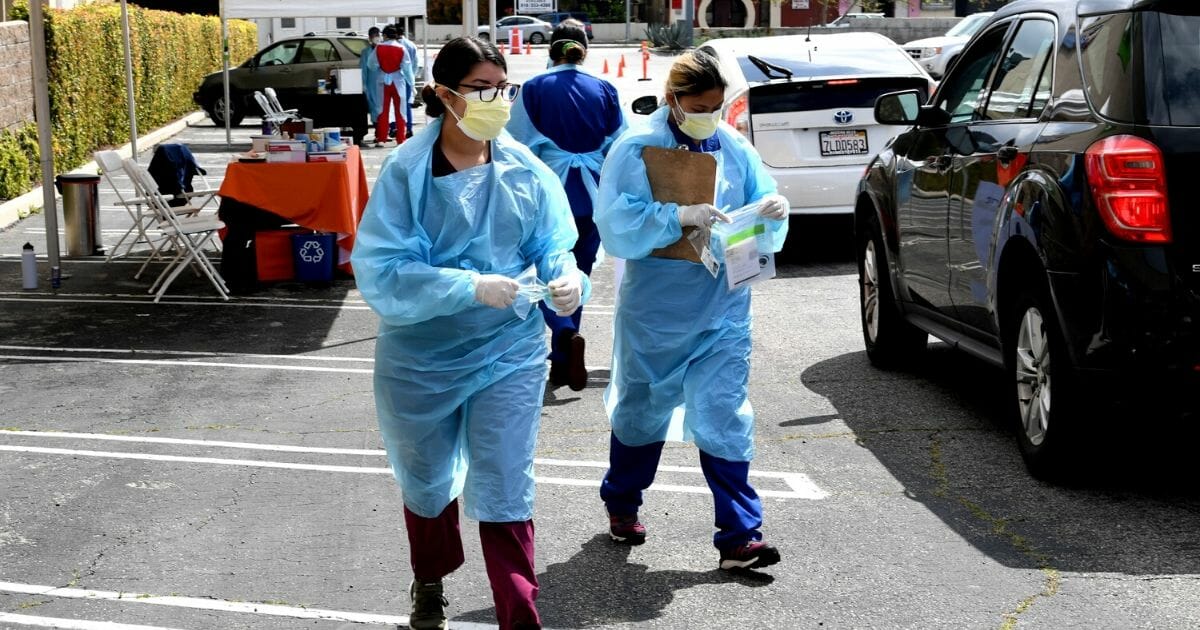 Workers wearing personal protective equipment gather the tests from people's cars administered as Mend Urgent Care conducts drive-thru testing for COVID-19 at the Westfield Fashion Square on April 13, 2020, in the Sherman Oaks neighborhood of Los Angeles, California.