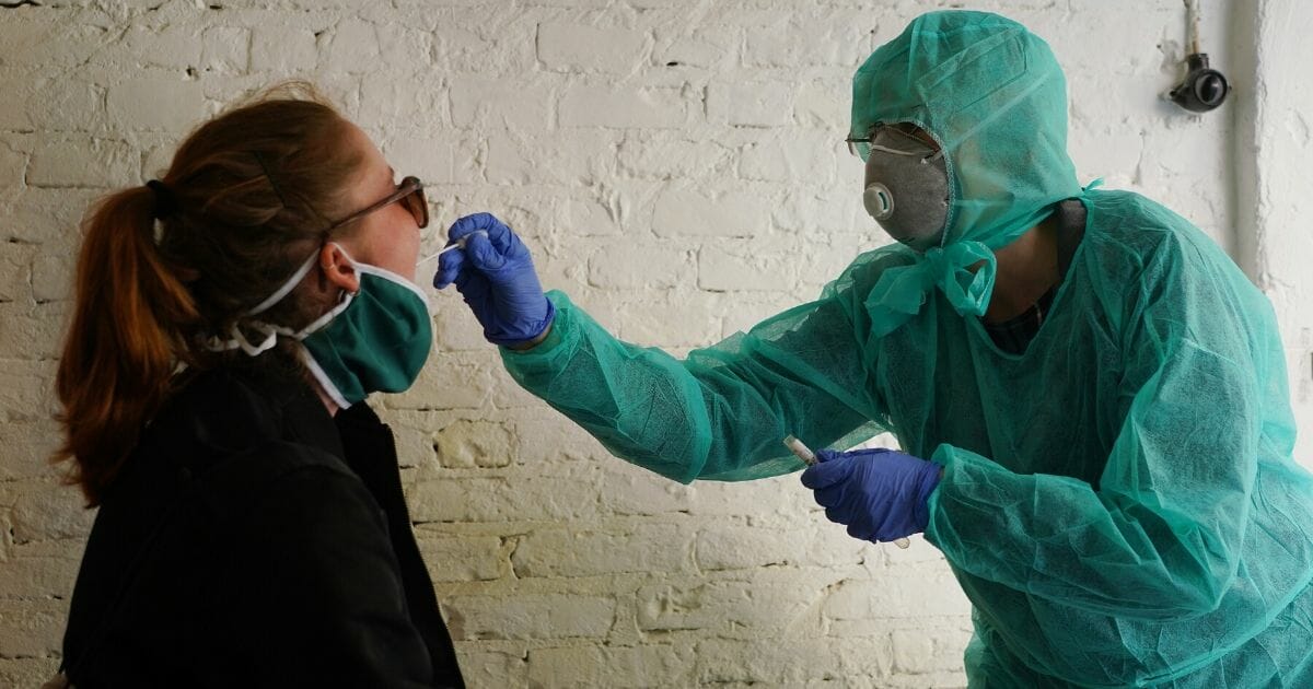 Doctor Beate Krupka, dressed in a protective suit and mask, takes a throat swab from a young woman to test her for COVID-19 in a garage behind Krupka's practice during the coronavirus crisis on April 8, 2020, in Berlin, Germany.
