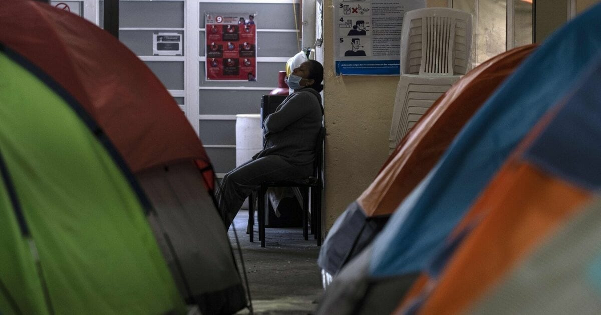 A woman rests near posters with information on the prevention of COVID-19 at the Juventud 2000 migrant shelter in Tijuana, Mexico, on April 3, 2020.