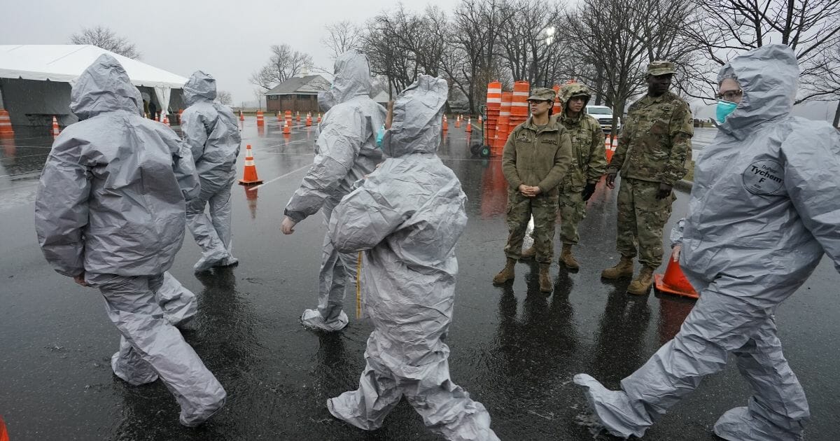 Workers in protective suits get ready while waiting for people to be tested for COVID-19 as they arrive by car at Glen Island Park in New Rochelle, New York, on March 13, 2020.