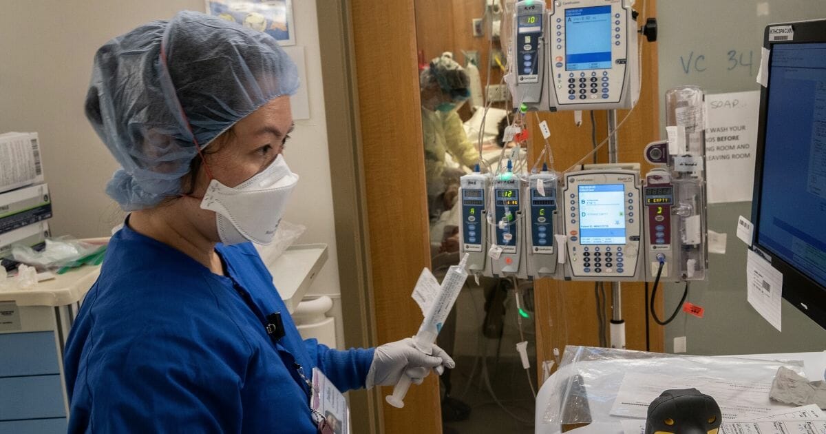 A nurse wearing an N95 mask works as intravenous therapy equipment hangs outside a COVID-19 patient's door in the intensive care unit at Stamford Hospital in Stamford, Connecticut, on April 24, 2020.