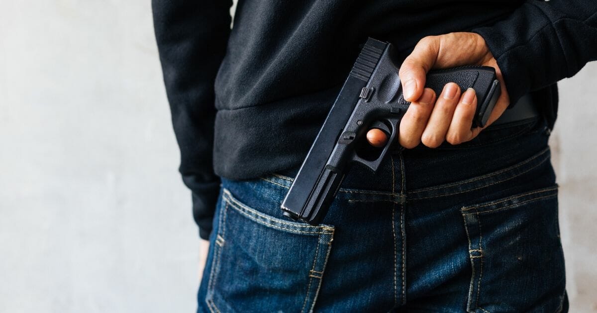 A man's hand holding a gun behind his back.