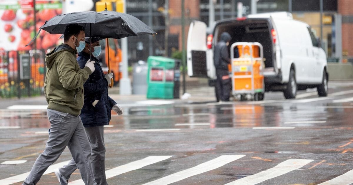 Two people walk in the rain wearing protective masks and gloves on April 21, 2020, in New York City.