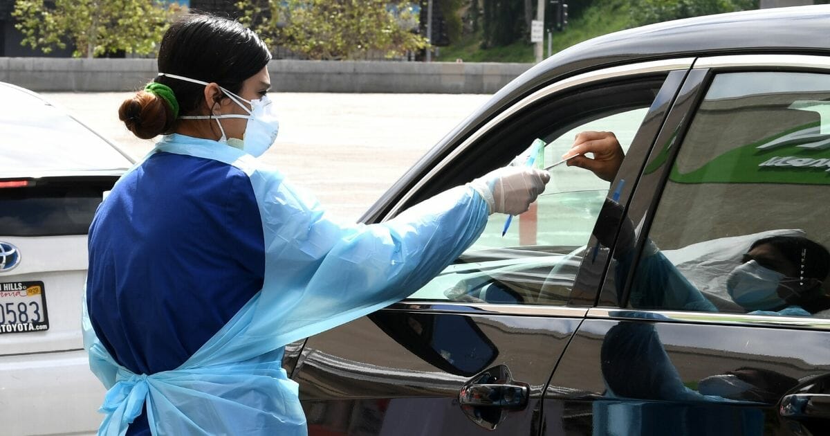 A worker wearing personal protective equipment gathers the tests administered from a car as Mend Urgent Care conducts drive-thru testing for COVID-19 at the Westfield Fashion Square on April 13, 2020, in the Sherman Oaks neighborhood of Los Angeles, California.