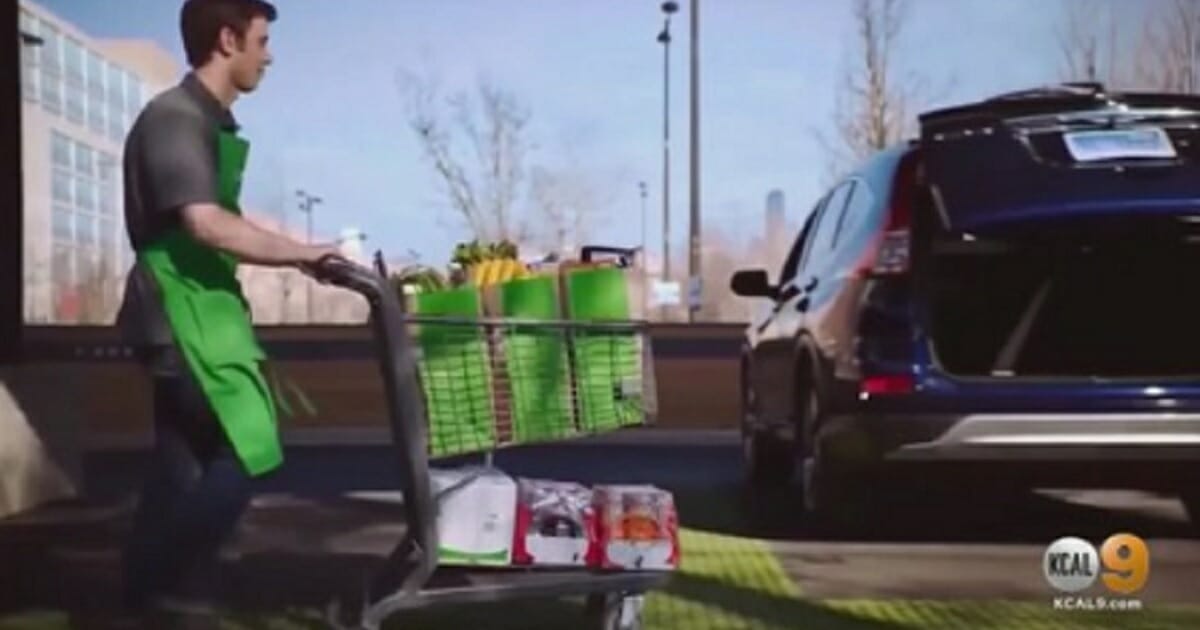 A grocery worker pushes a shopping cart full of goods to a waiting vehicle.