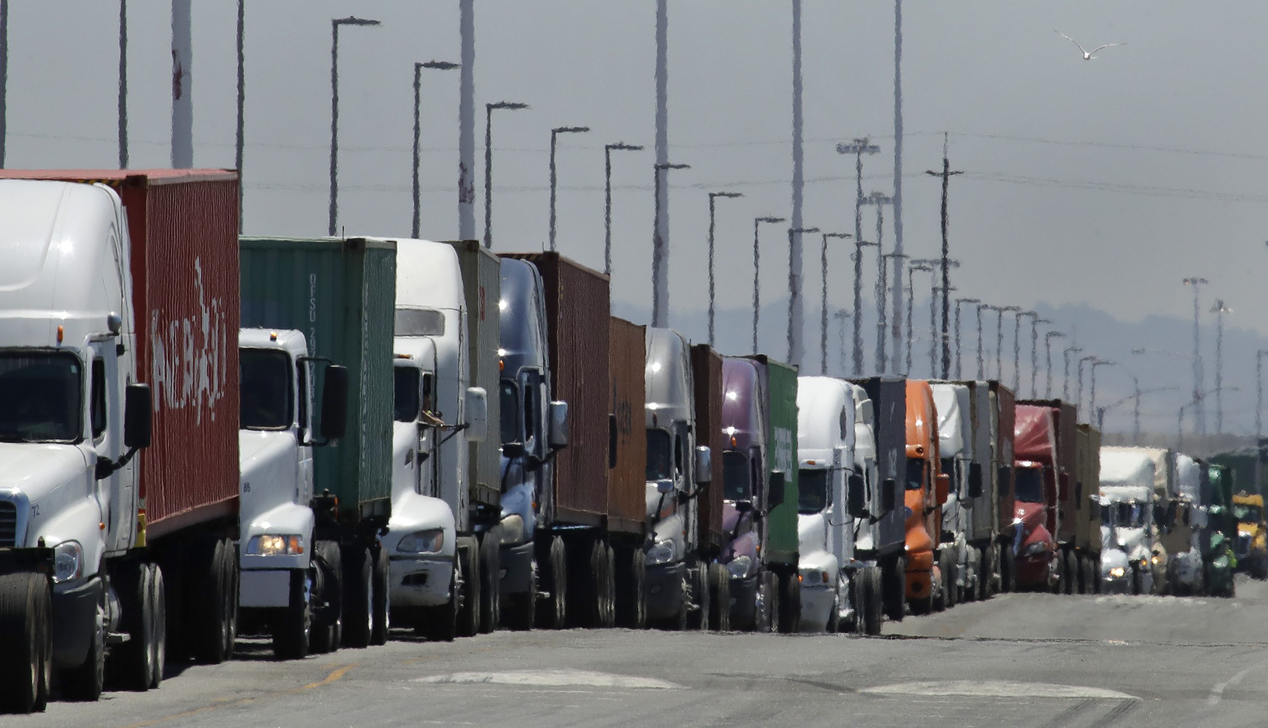 In this July 22, 2019, photo, trucks hauling shipping containers wait to unload at the Port of Oakland in Oakland, California.