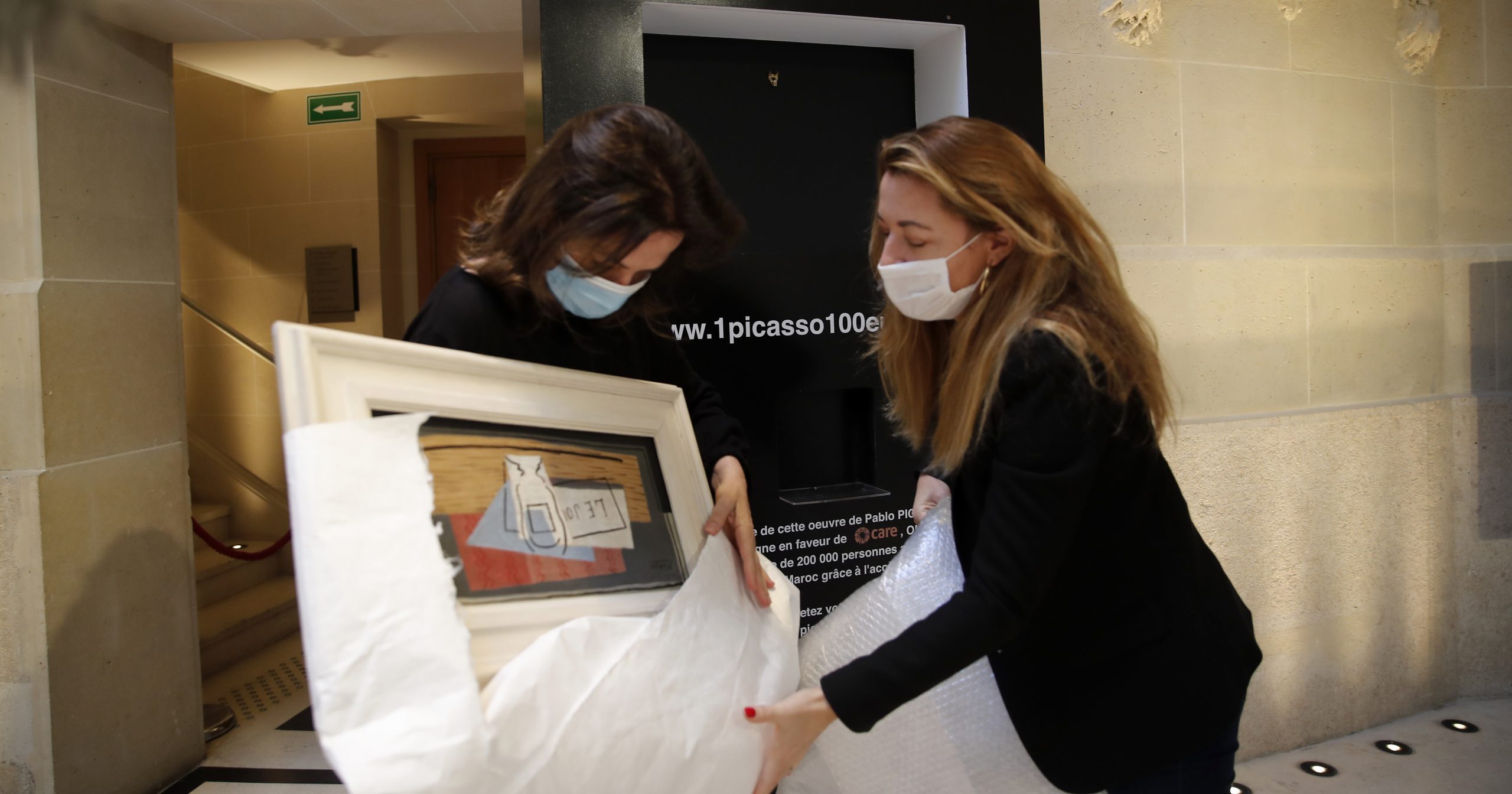 Raffle organizers Peri Cochin, left, and Arabenne Reille unbox the painting "Nature morte" by Picasso at Christie's auction house on May 19, 2020, in Paris.