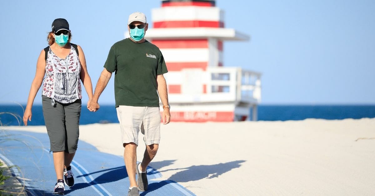 A couple wear protective masks as they walk in South Pointe Park in Miami Beach, Florida, on April 29, 2020.