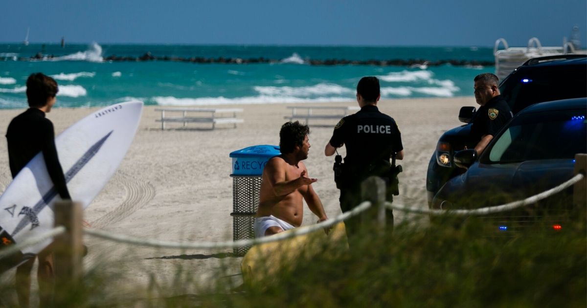 Police officers detain a man who was spotted on the closed South Beach of Miami Beach, Florida, on March 19, 2020.