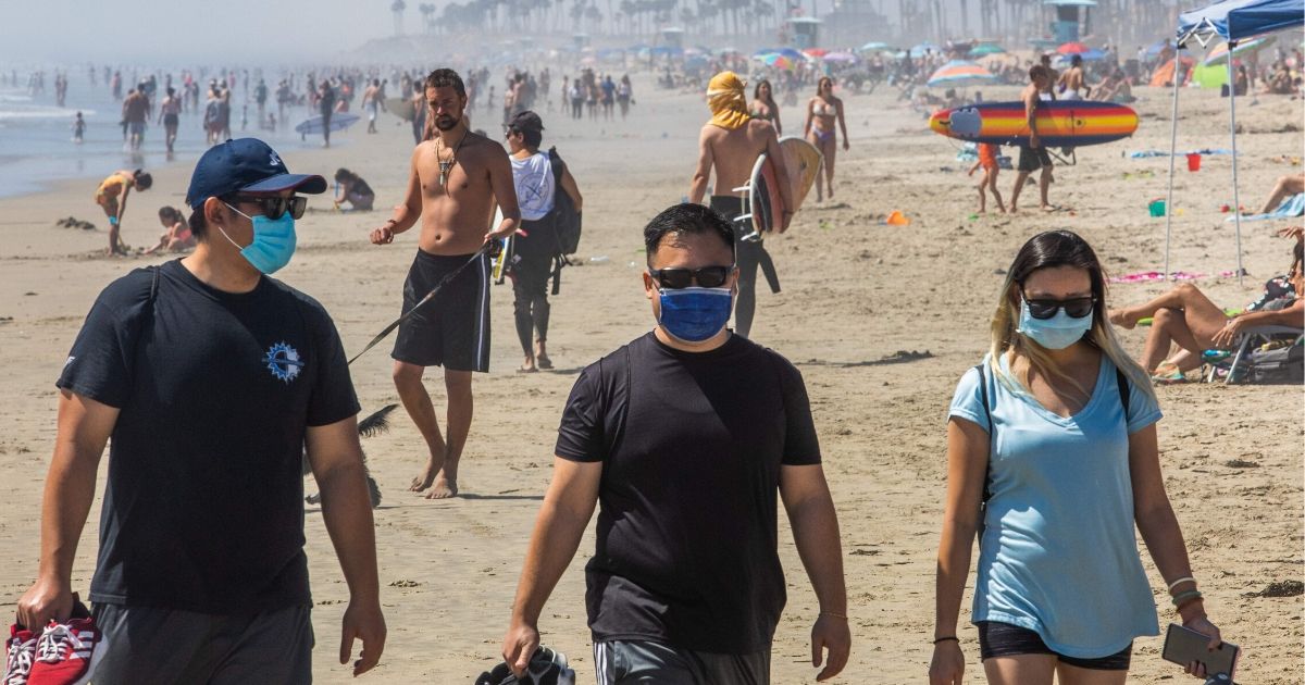 People walk on the beach, some wearing masks, amid the novel coronavirus pandemic in Huntington Beach, California, on April 25, 2020.