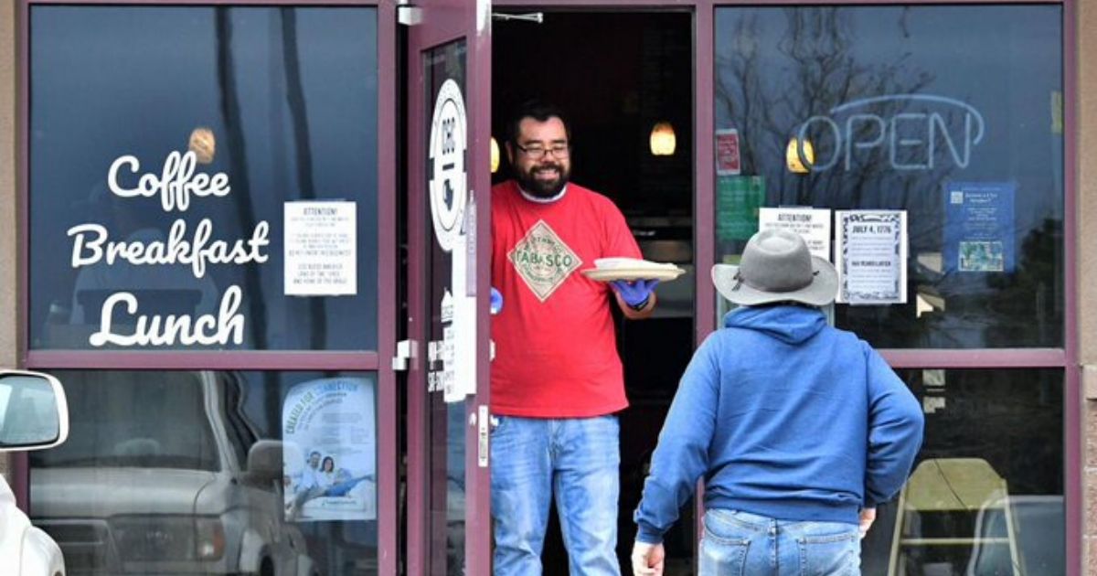 Jesse Arellano hands a breakfast burrito to his friend and regular, Robert Taylor, from the front door of his restaurant, C&C Coffee and Kitchen in Castle Rock, Colorado, on May 11, 2020.