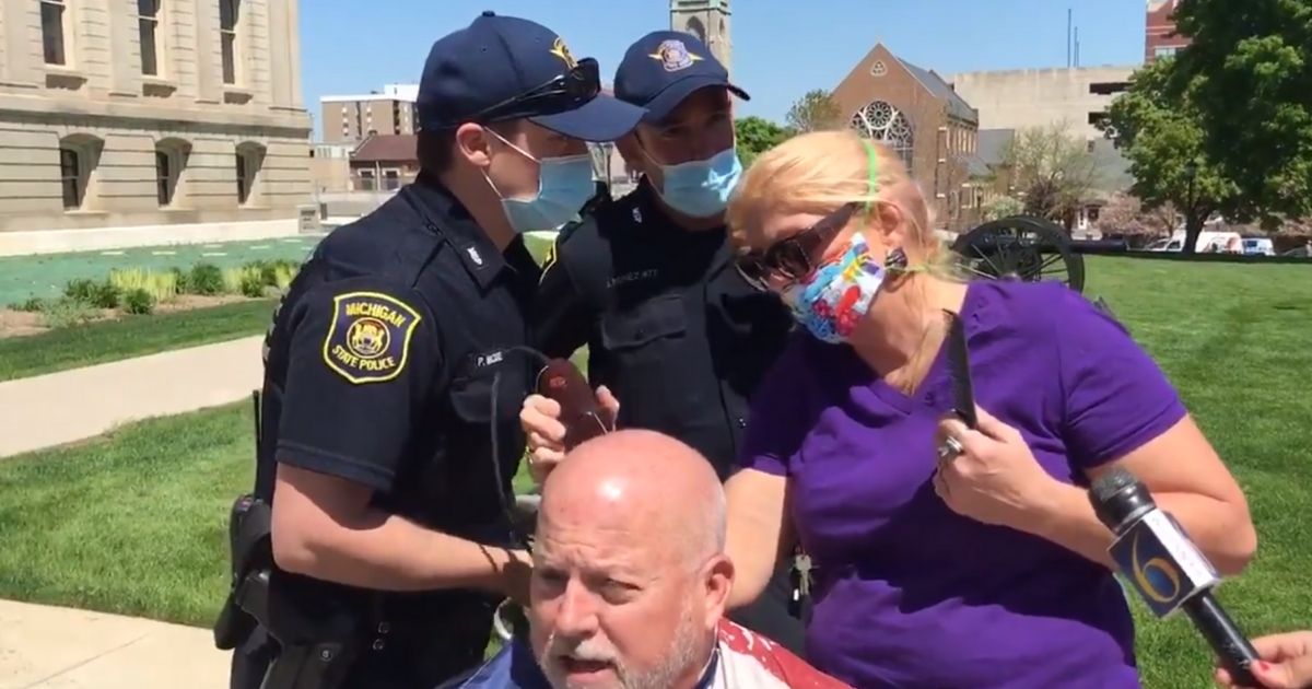 Michigan state troopers confront a woman cutting hair in front of the state Capitol in Lansing.