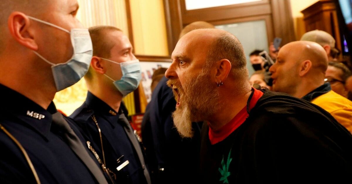 Brian Cash and other protesters are face to face with state troopers during a rally to reopen businesses at the Michigan State Capitol in Lansing on April 30, 2020.