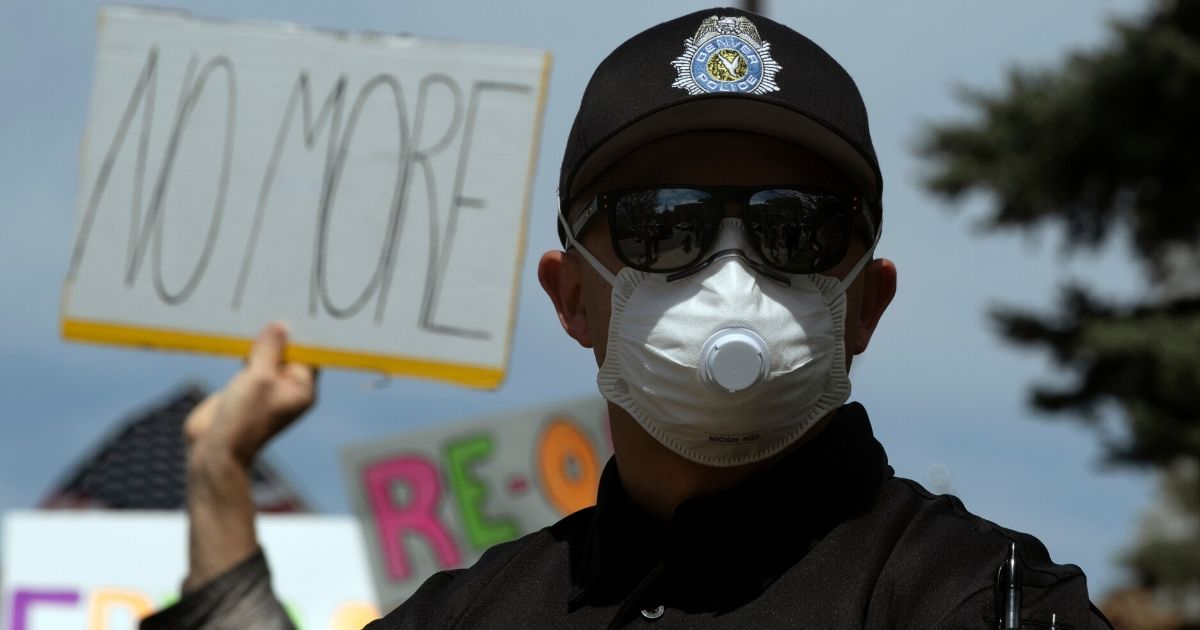 A police officer wearing a face mask stands by as demonstrators gather to protest coronavirus stay-at-home April 19, 2020, in Denver.