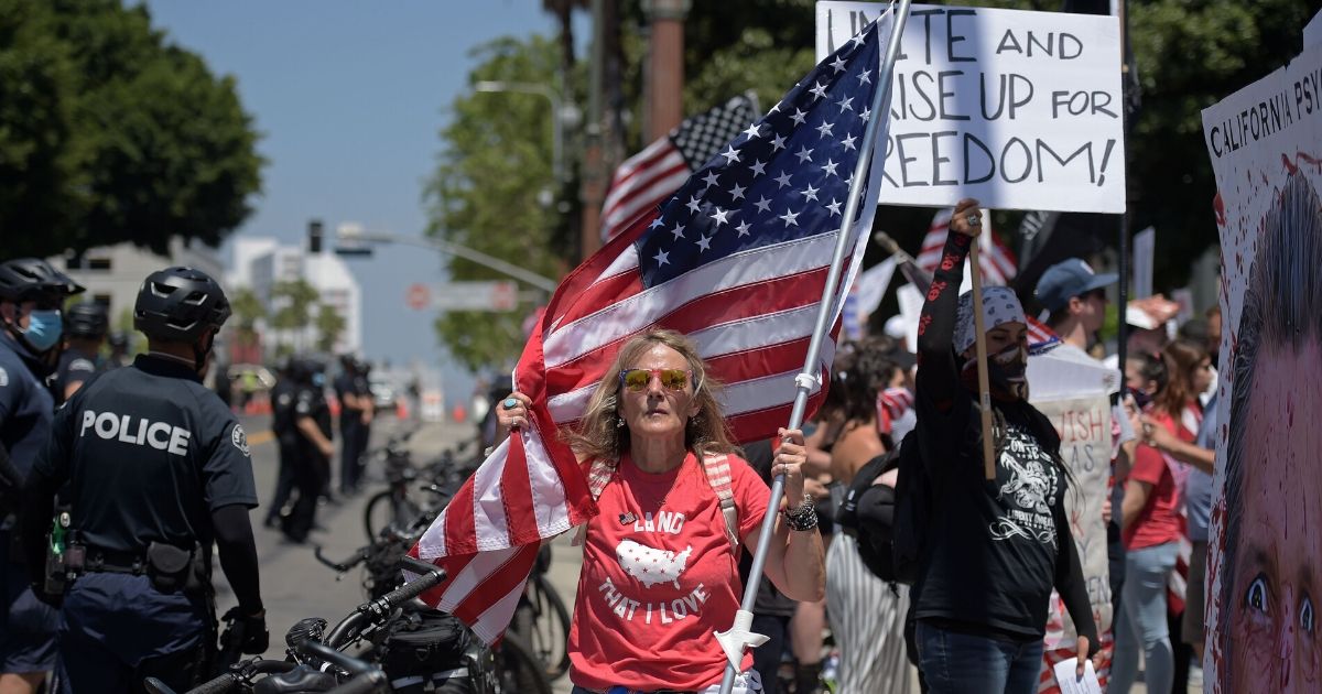 A woman holds a American flag as people gather to protest the stay-at-home orders still in effect near Los Angeles City Hall on May 1, 2020.