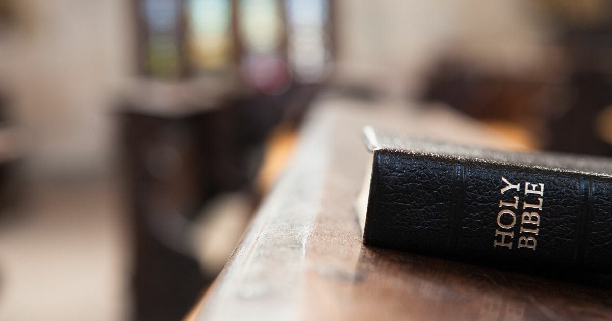 Stock image of a Bible resting on a wooden church bench.