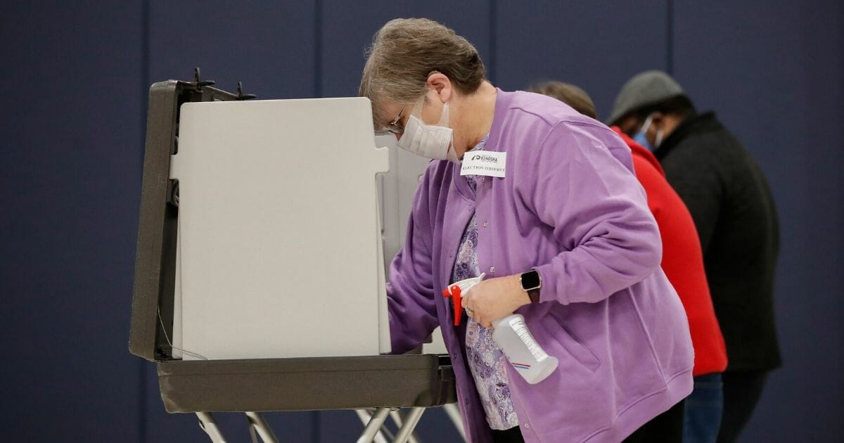 An election observer cleans a voting booth during Democratic presidential primary voting at the Kenosha Bible Church gym in Kenosha, Wisconsin, on April 7, 2020.