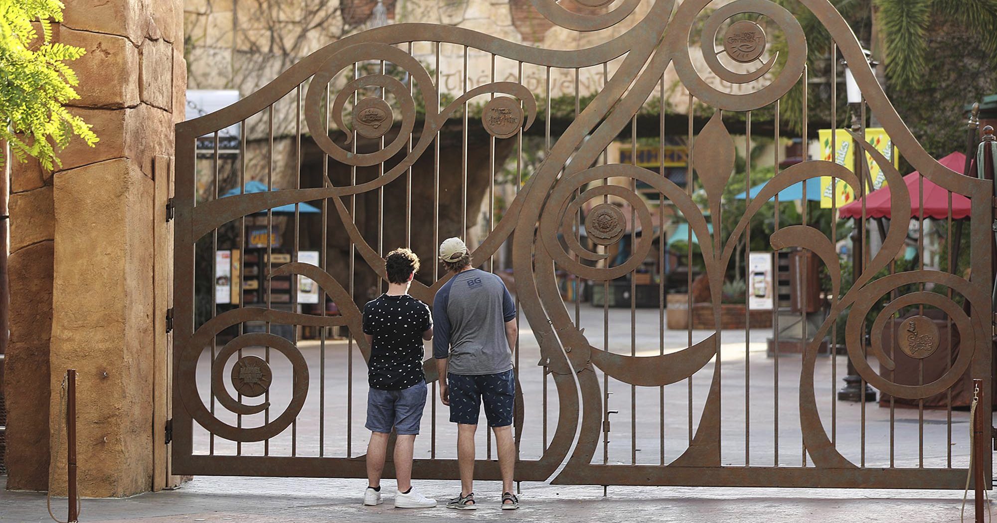 In this May 14, 2020, file photo, guests peer through the closed gate to Universal's Islands of Adventure beside Universal CityWalk, in Orlando, Florida.