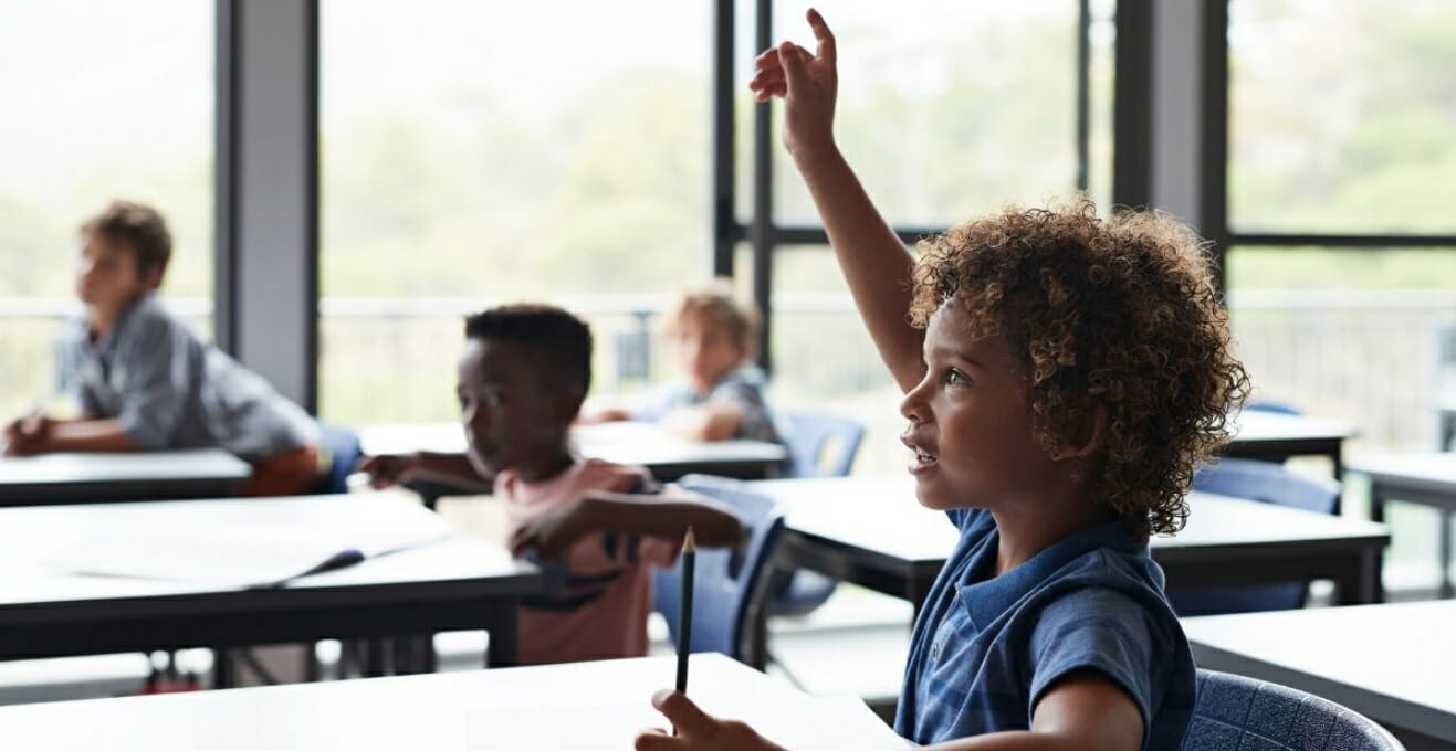 A child in school with a hand up to be called on.