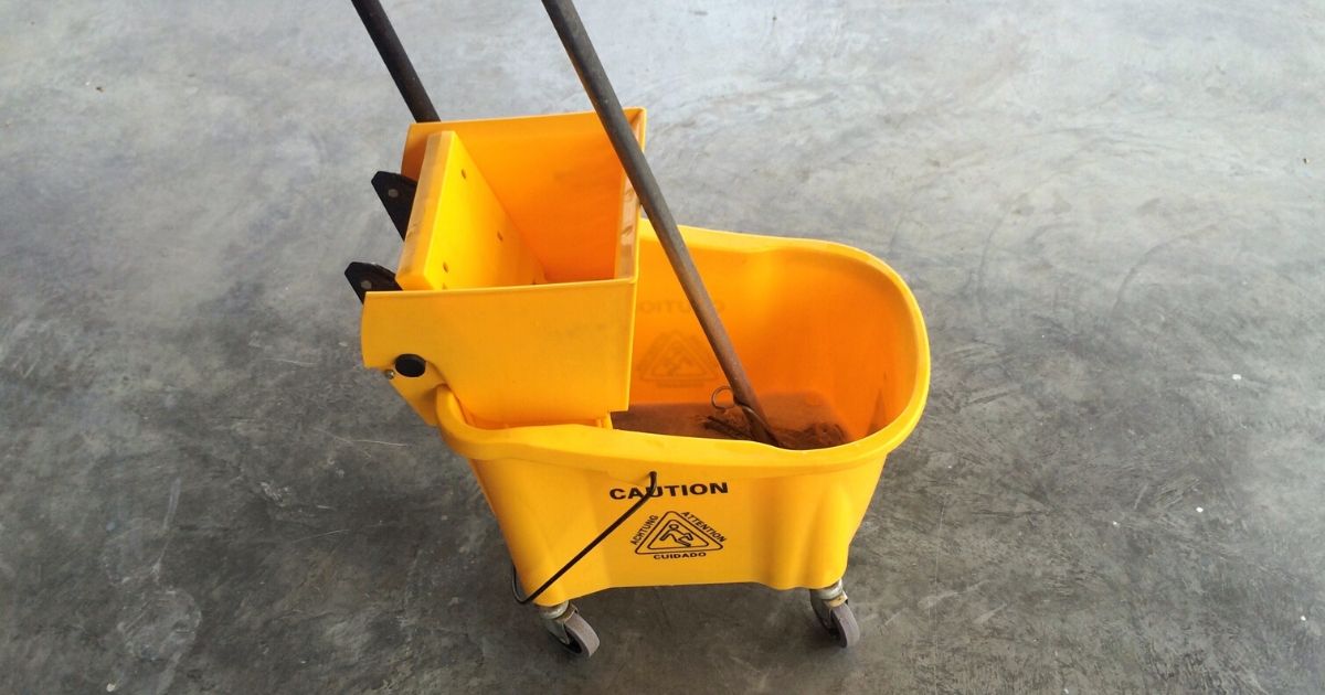 An industrial mop and bucket on bare cement.