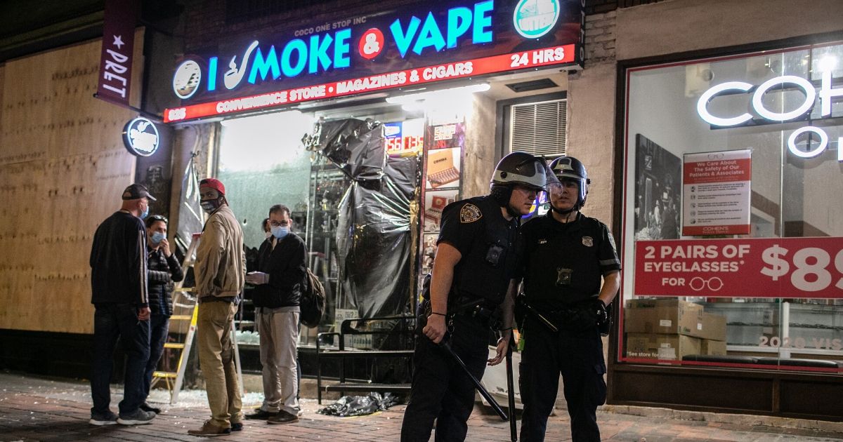 New York City police officers stand guard near a looted vape shop during a night of protests and vandalism Monday.