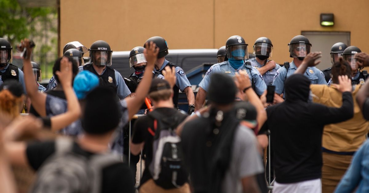 Police officers stand in a line while facing protesters outside the Third Police Precinct in Minneapolis on May 27, a day before the precinct was overrun and burned by rioters.