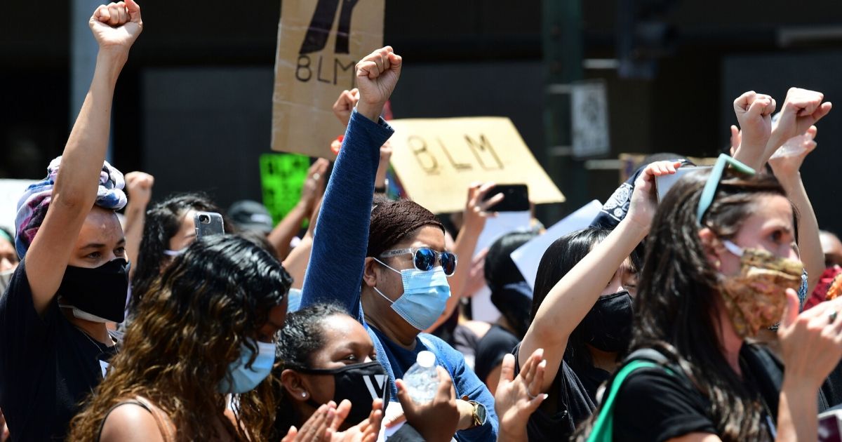 People hold up their fists during a memorial service honoring George Floyd in downtown Los Angeles on June 8, 2020.