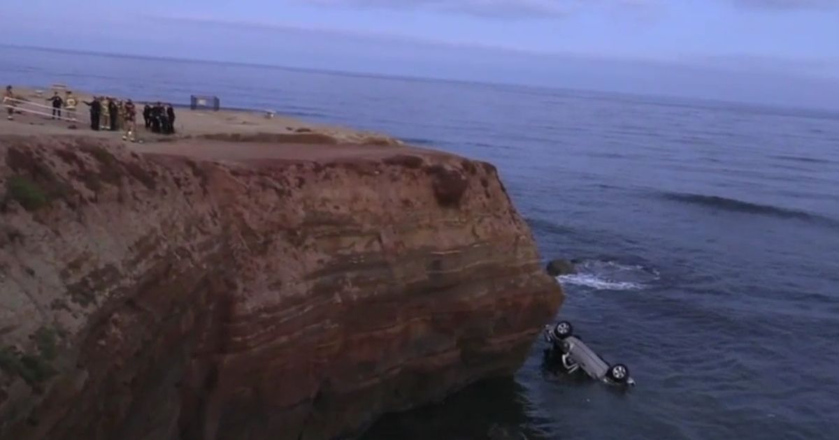 Police officers stand on a cliff near the scene where a man drove a truck off a cliff in San Diego.